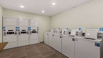 A laundry facility with multiple washing machines and dryers, arranged in rows.