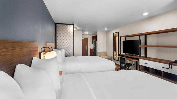A modern hotel room with a large bed, a desk with a computer, a TV, and a seating area with a chair and a sofa. - Everhome Suites Bastrop By Choice Hotels (Bastrop)