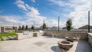 An outdoor patio area with a barbecue grill, stone planters, and string lights. - Everhome Suites Bastrop By Choice Hotels (Bastrop)