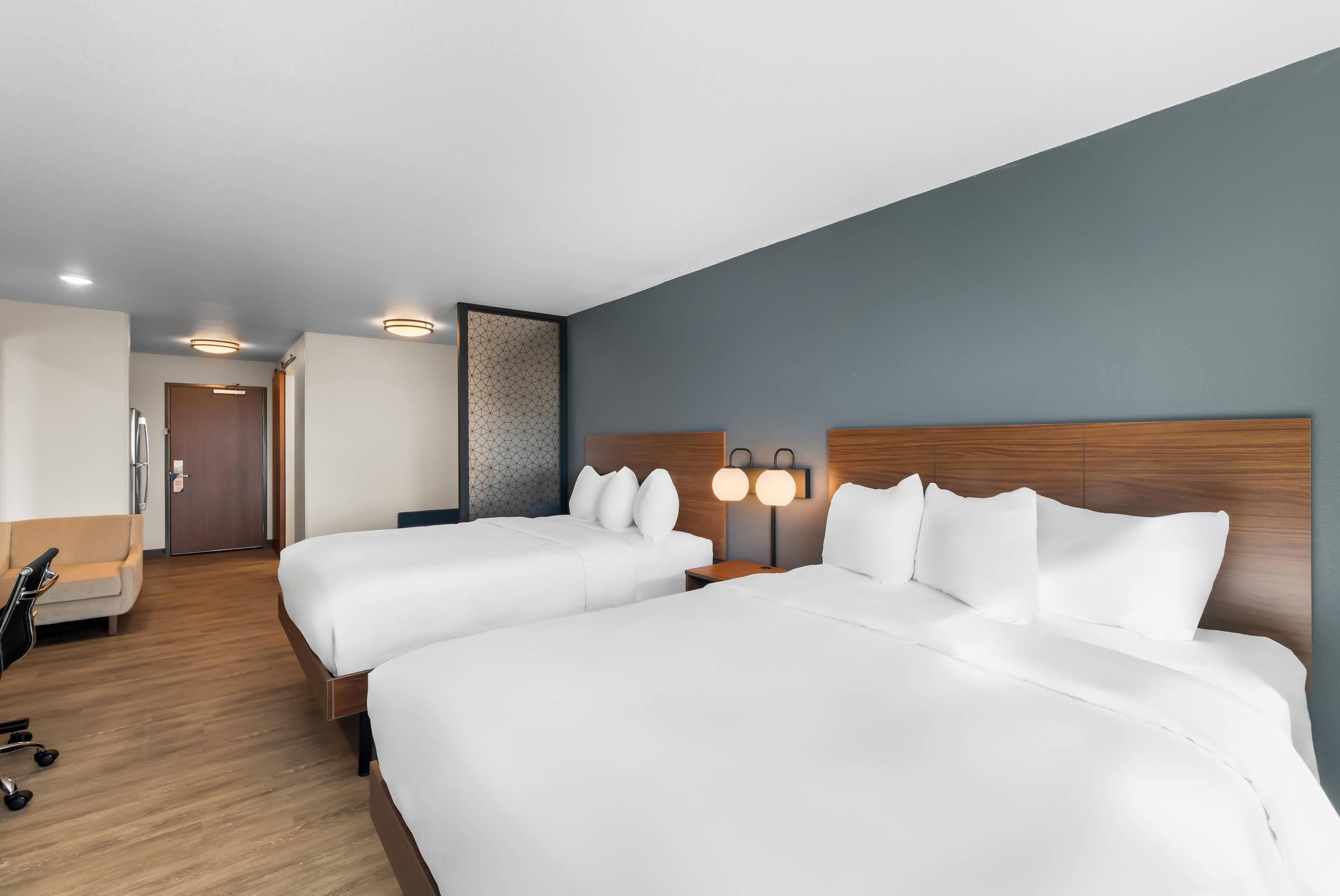 A hotel room with two beds, a desk, a chair, and a door.