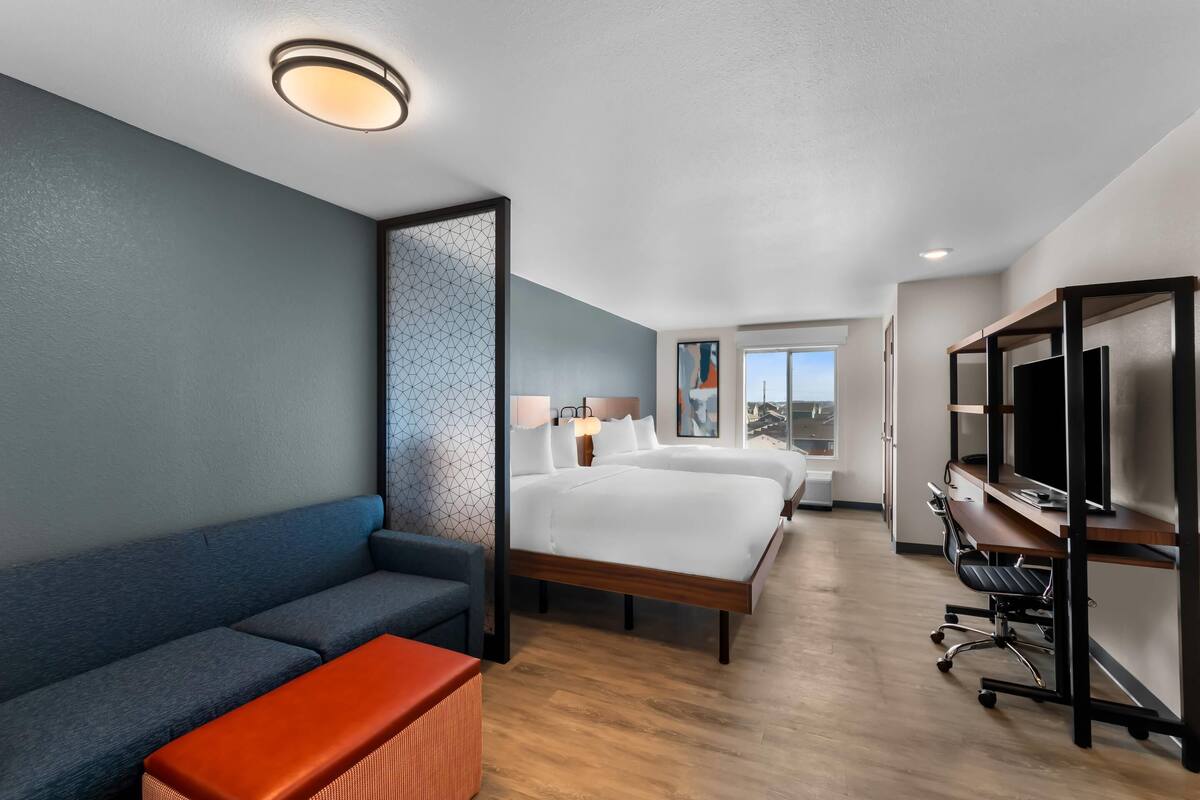 A hotel room with a sofa, two beds, a desk, and a TV.