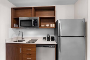 Una cocina moderna con microondas integrado, horno y refrigerador, lavavajillas y armarios de madera.