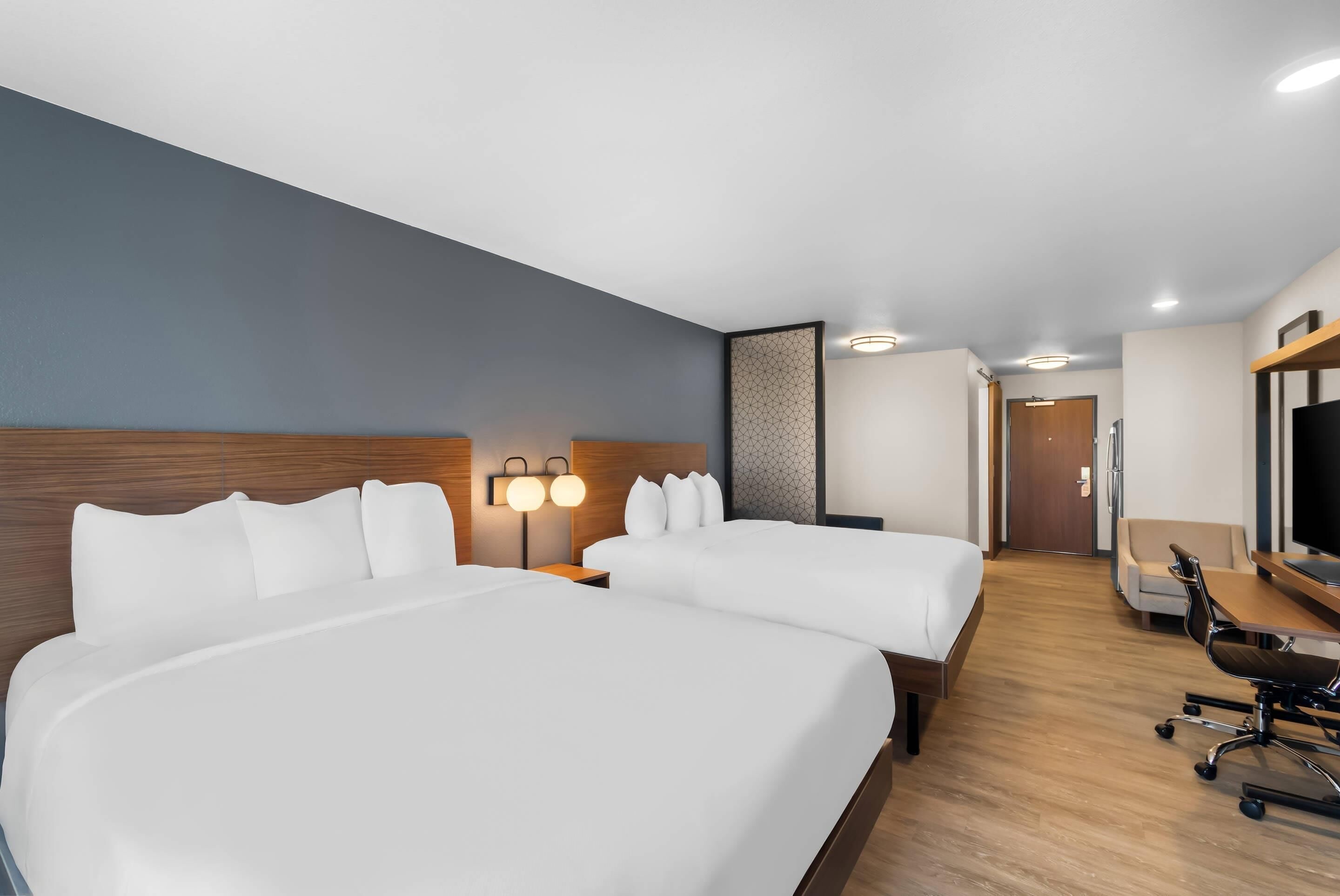 A hotel room with two beds, a desk, a chair, and a TV.
