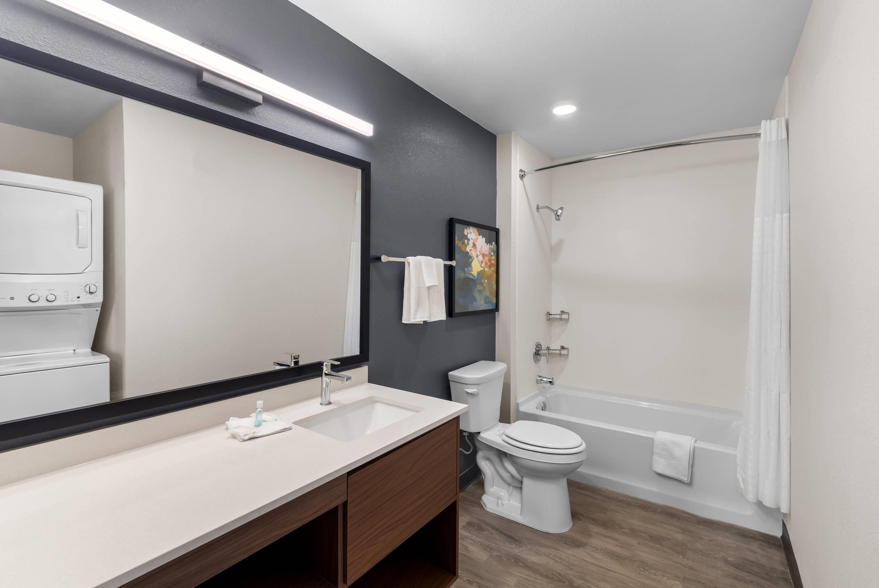 A modern bathroom with a large mirror, a sink, a toilet, and a bathtub.