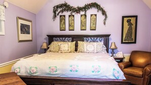 Une chambre à coucher avec un grand lit, une literie à motifs floraux, une tête de lit en bois et un fauteuil en cuir marron.