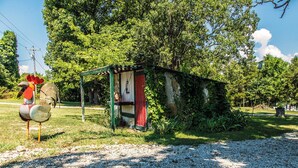 Une construction rustique en bois, dotée d’une porte rouge, entourée d’une végétation luxuriante et d’arbres.