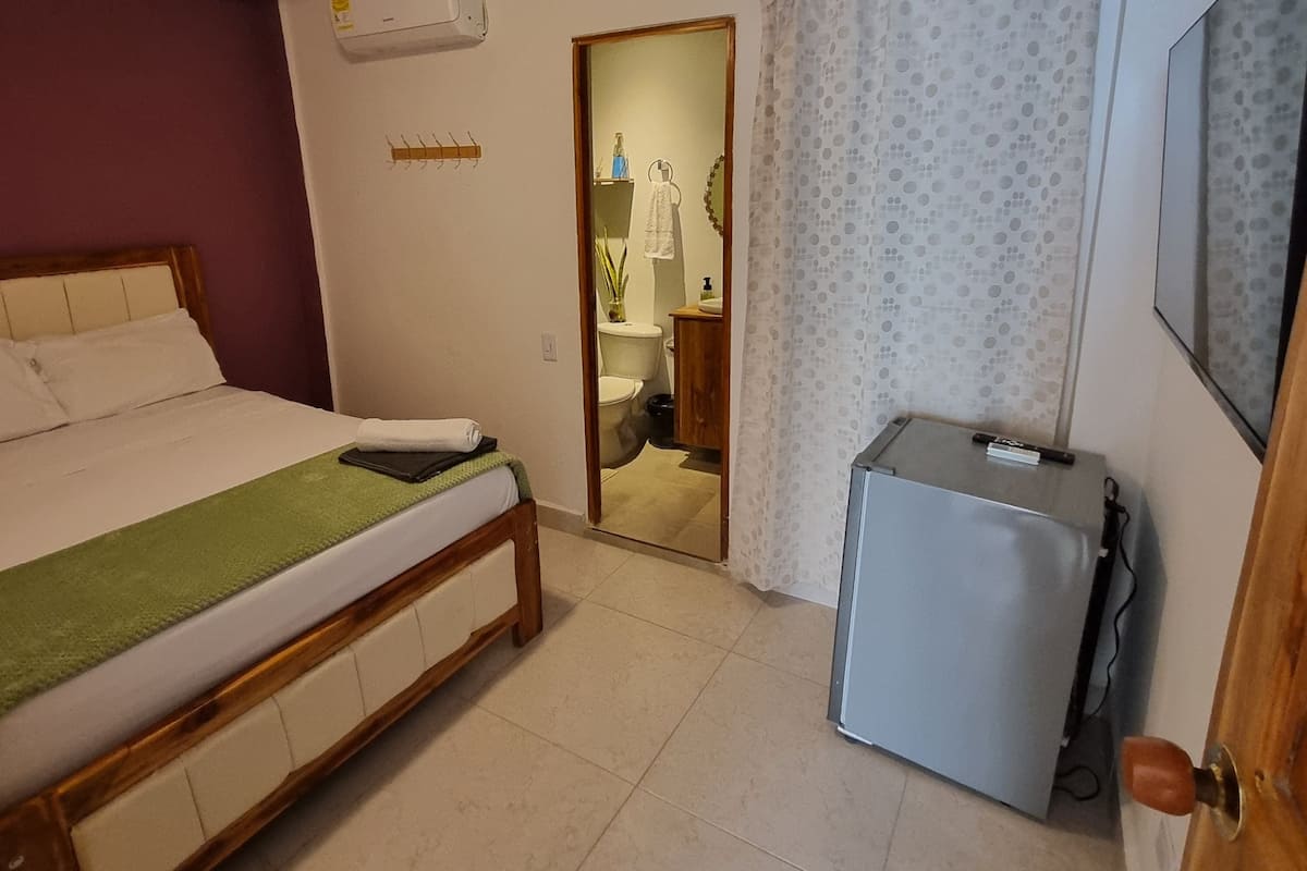 Une chambre avec un lit, un petit réfrigérateur, une salle de bain avec des toilettes et un rideau de douche.