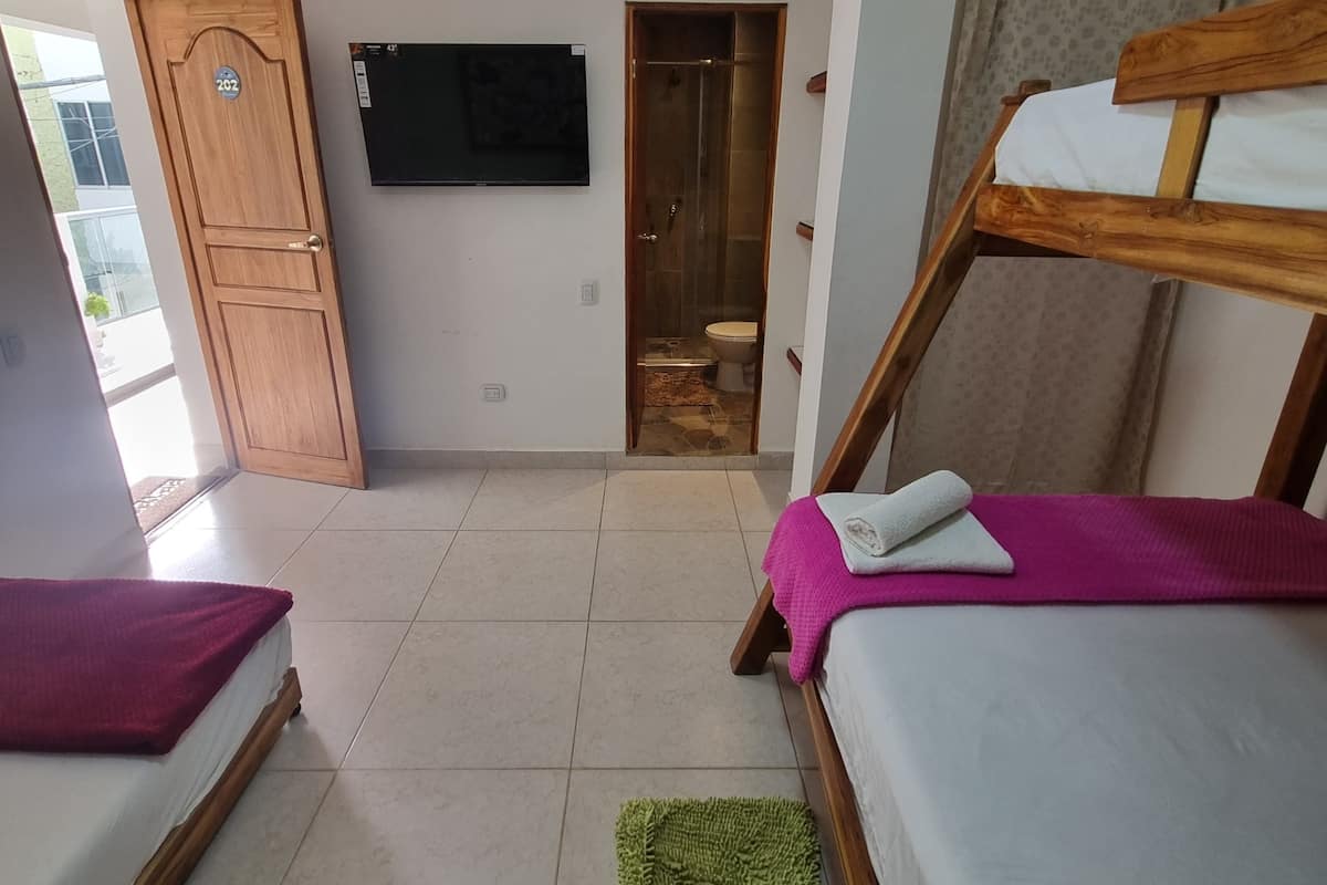 Une chambre avec deux lits, une télévision, une porte en bois et une salle de bain visible à travers une porte ouverte.