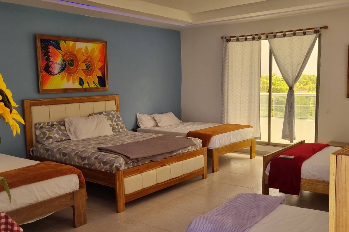 Une chambre d’hôtel avec deux lits en bois, un grand tableau représentant des fleurs, un luminaire au plafond et une fenêtre avec des rideaux.