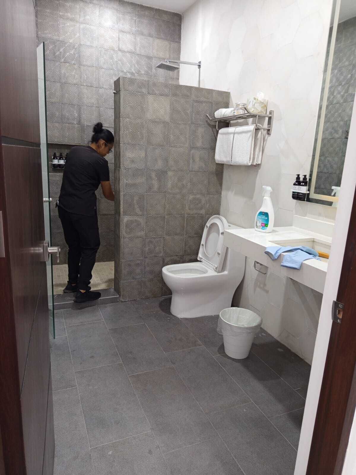 Une salle de bain avec des toilettes, une douche et un lavabo. On peut voir une personne debout près de la douche.