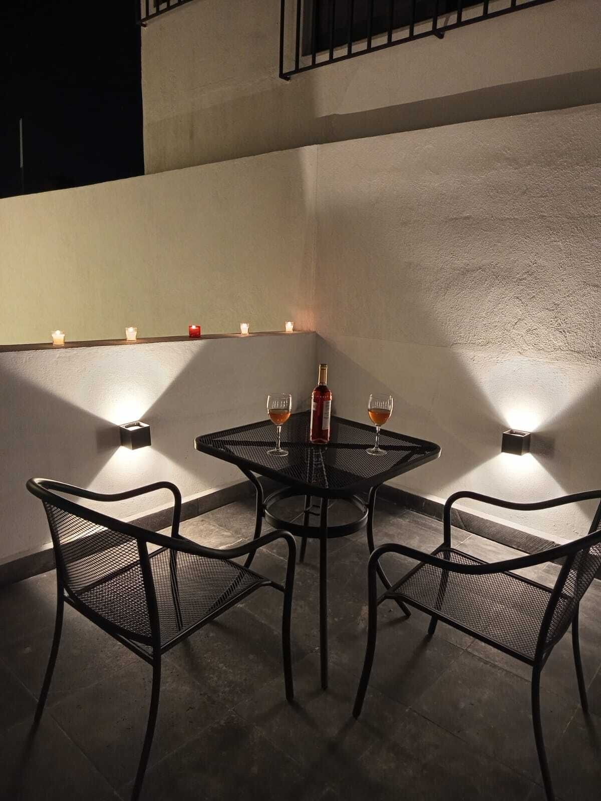 Un pequeño espacio al aire libre con una mesa, sillas, velas y una botella de vino.