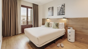 Hotelkamer met een groot bed, houten vloer, gordijnen, een nachtkastje met een klok en kunst aan de muur.