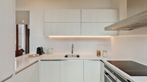 Uma cozinha moderna com armários brancos, uma pia de aço inoxidável e uma placa de indução.