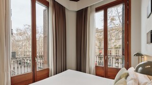 Quarto com cama grande, molduras de janela de madeira e vista para a cidade.