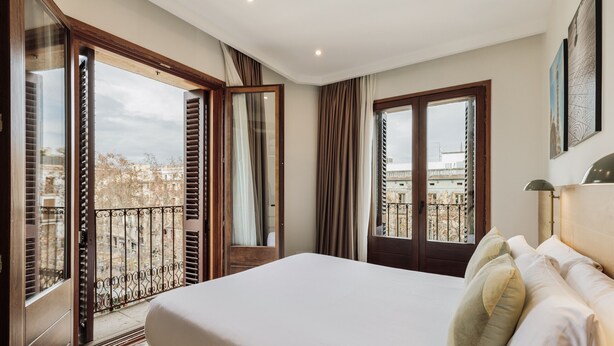 Ein Hotelzimmer mit einem großen Bett, einem Balkon mit Blick auf die Stadt und einer Tür zu einem Außenbereich.