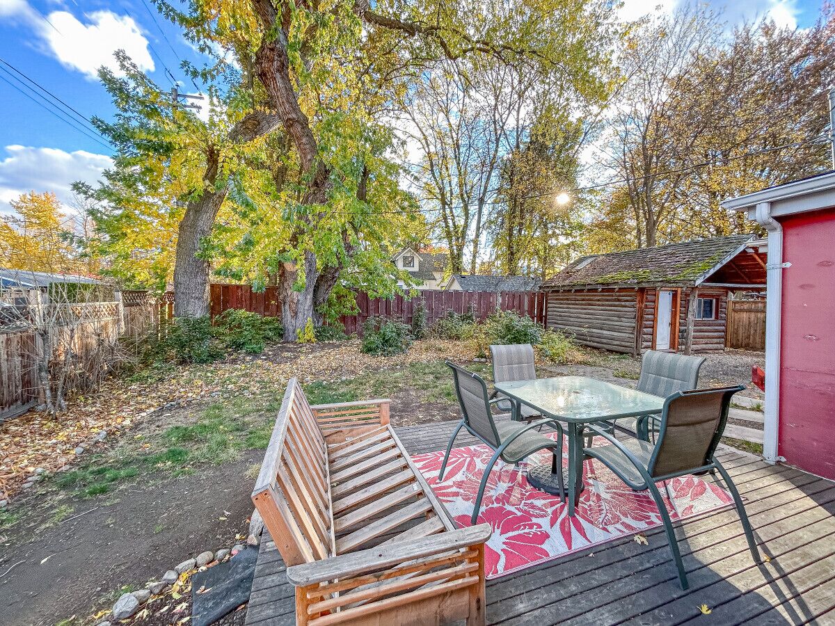 Une terrasse en bois avec une table et des chaises en verre, entourée d’une clôture en bois et d’arbres.