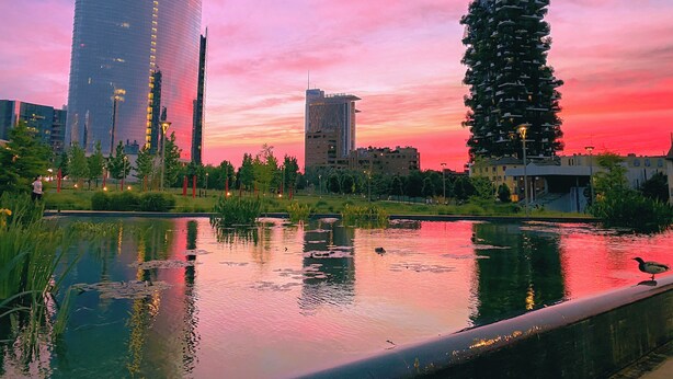 A modern urban landscape with a prominent UniCredit building, a unique cylindrical structure, and a calm water body reflecting the sunset. - Cardano Blue Suite - 5 min da Stazione Centrale (Milan)