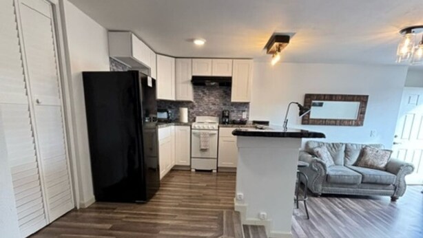 A modern kitchen with a black refrigerator, white cabinets, and a herringbone wood floor.