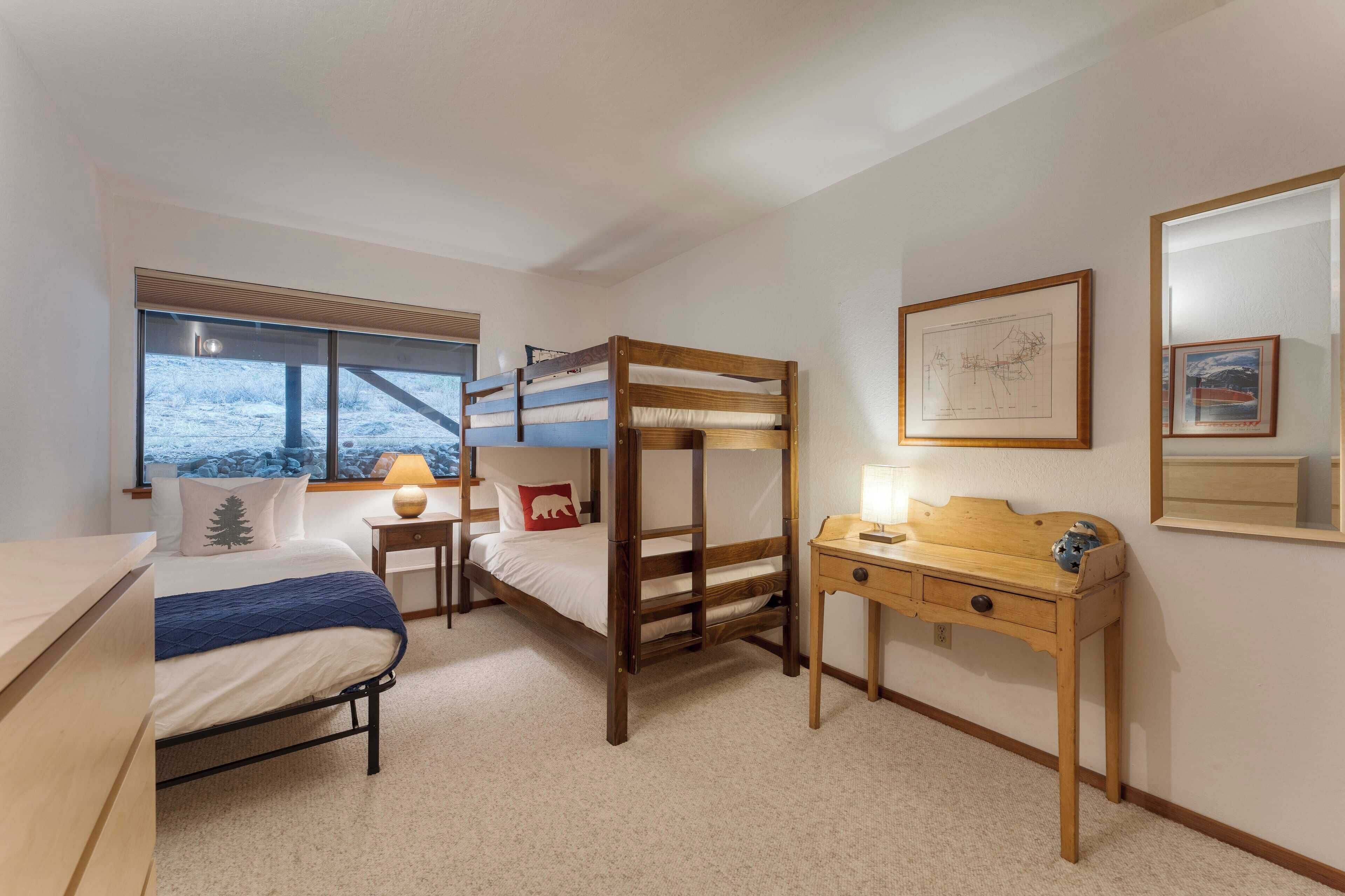 Ein Schlafzimmer mit einem Etagenbett, einem Schreibtisch, einer Lampe und einem Fenster mit Blick auf eine verschneite Landschaft.