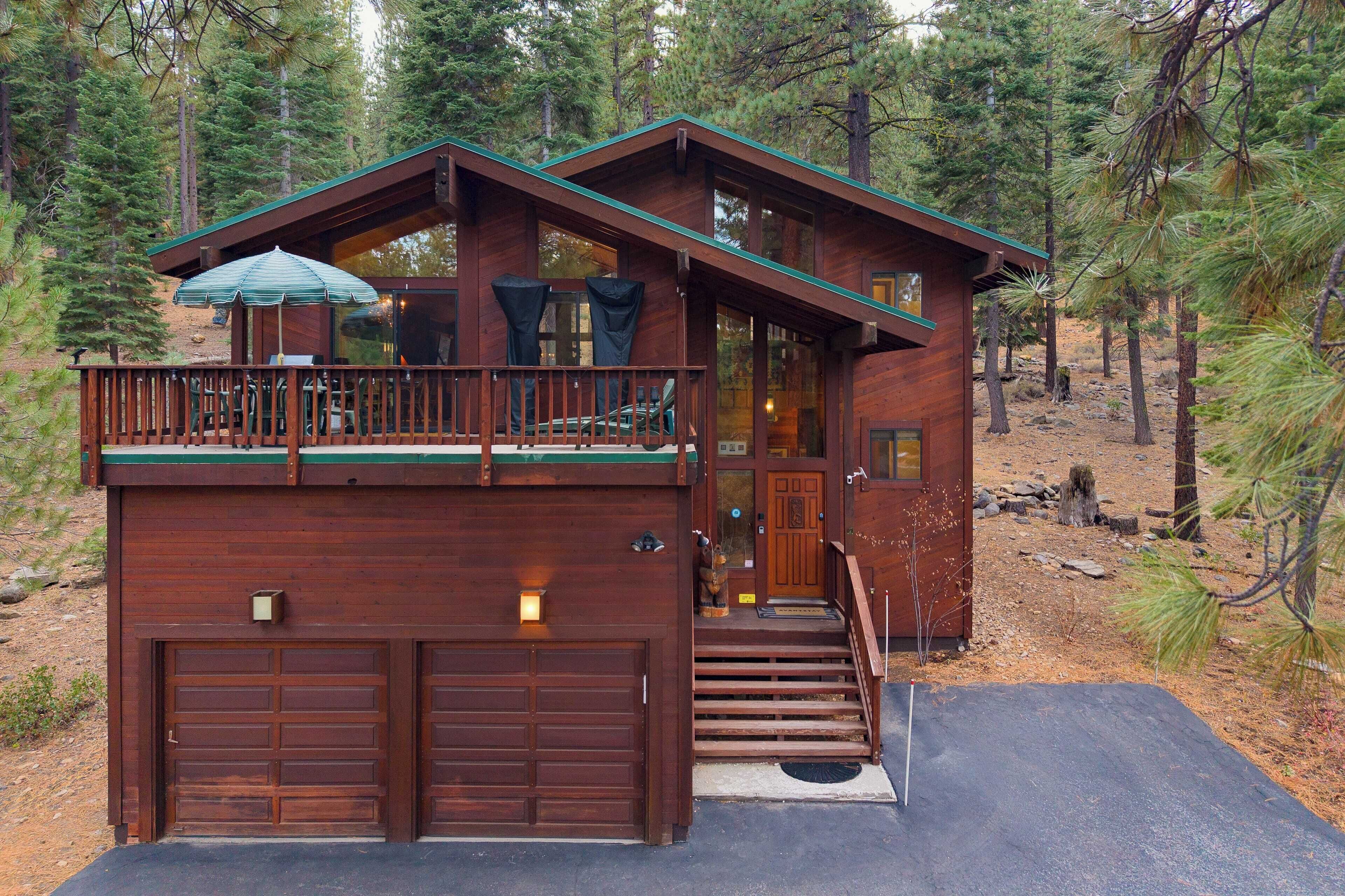 A cabin with a two-story structure, a balcony with a table and chairs, and a garage.