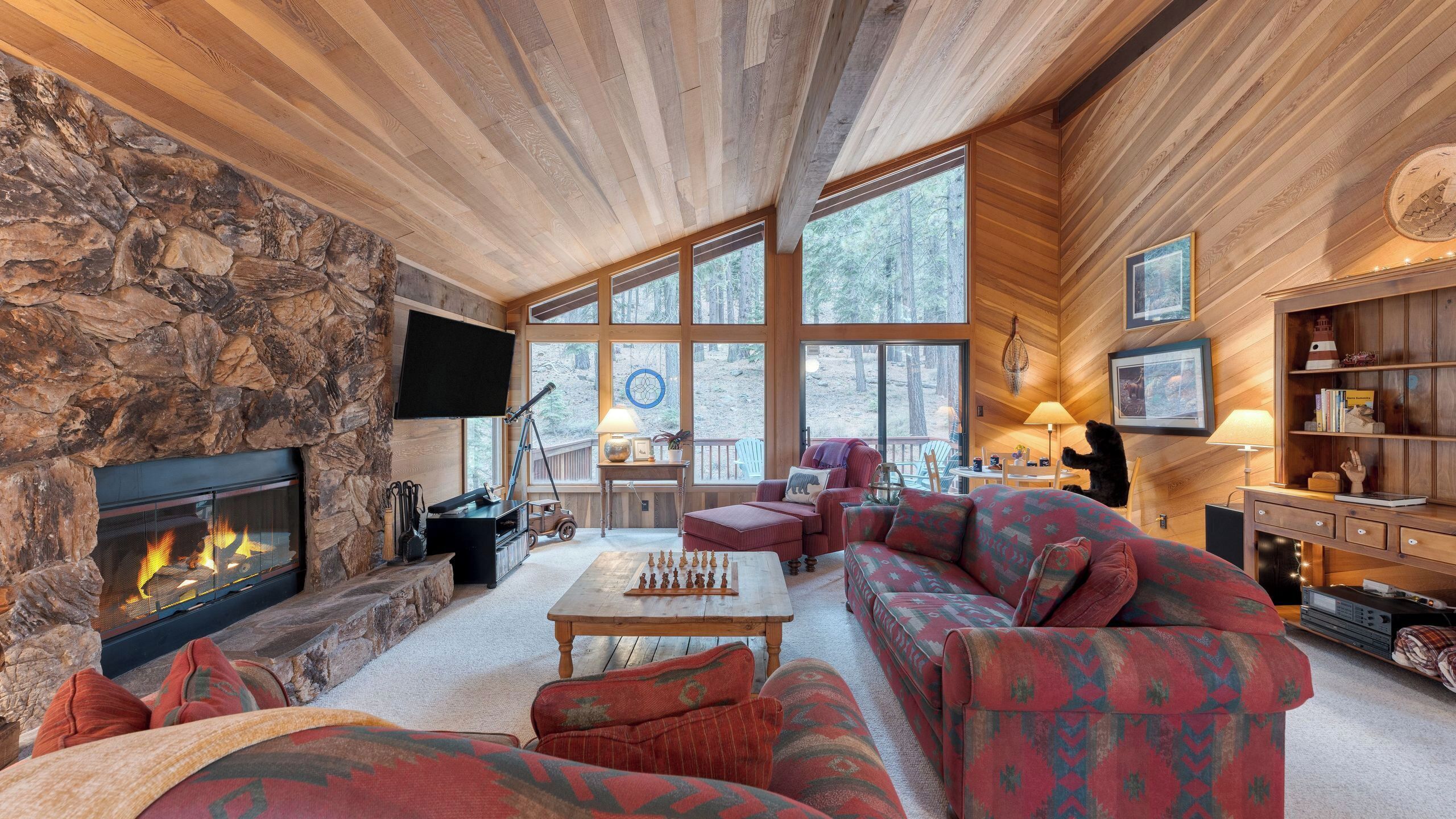 Een gezellig cabin interieur met een stenen openhaard, grote ramen, een houten plafond en een comfortabele zithoek.
