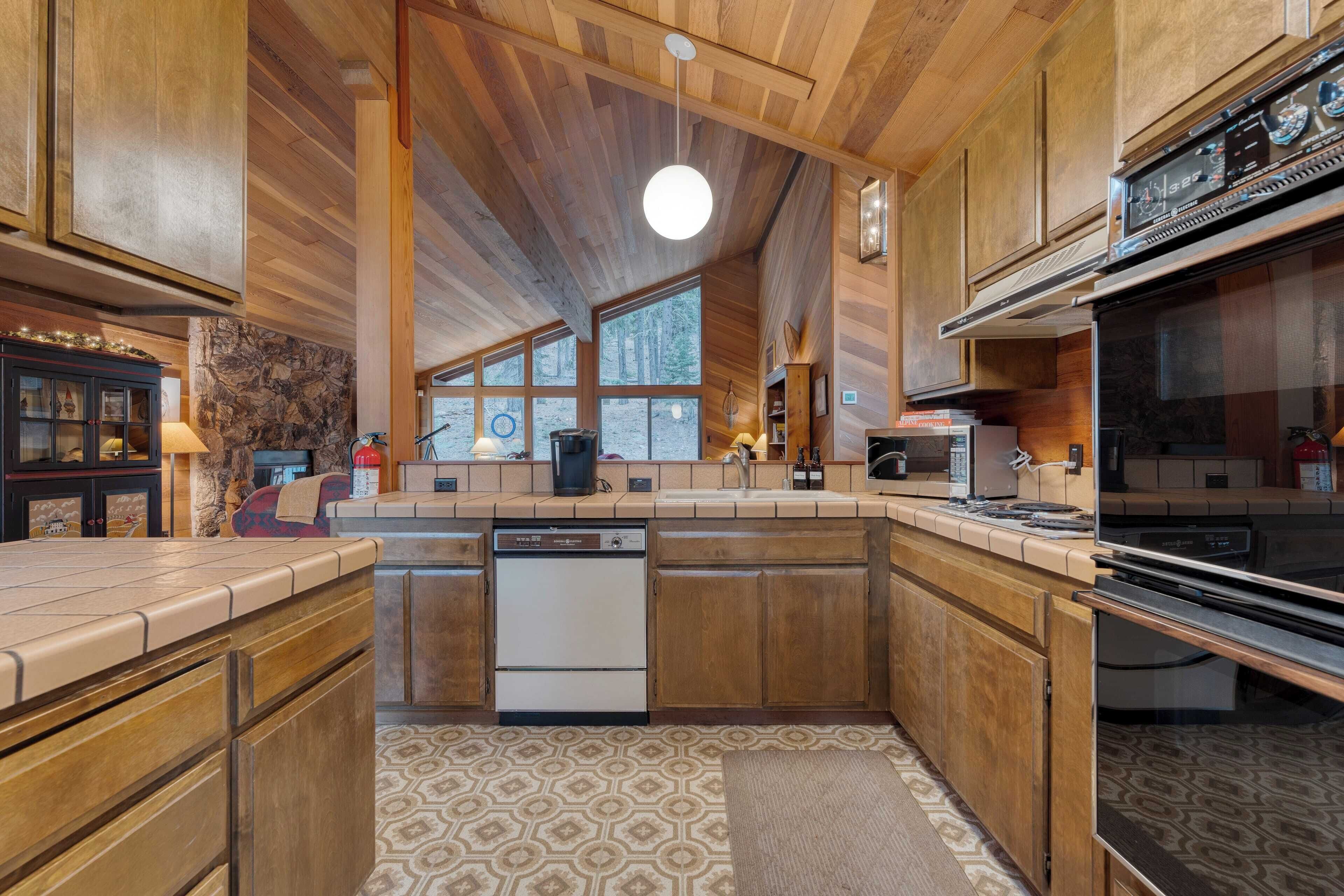 A spacious kitchen with wooden cabinets, a dishwasher, a stove, and a large window providing natural light.