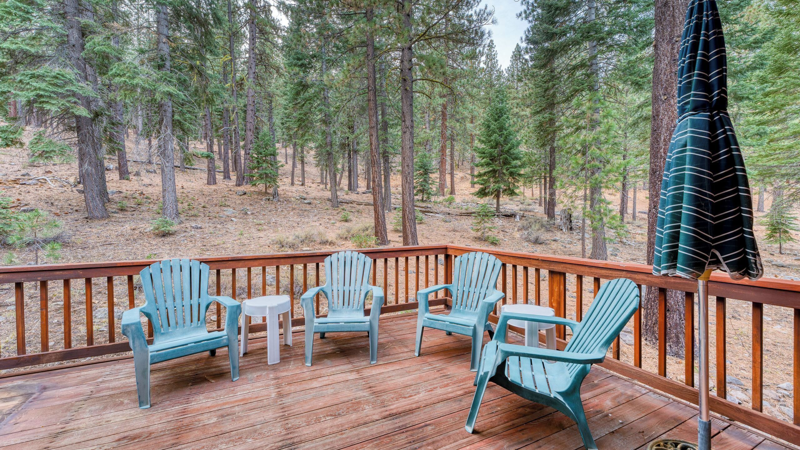 A wooden deck with four Adirondack chairs, a small table, and a blanket hanging on the railing.
