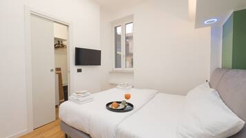 Una habitación de hotel moderna con una cama, un televisor montado en la pared, una ventana y una puerta que da a un baño.