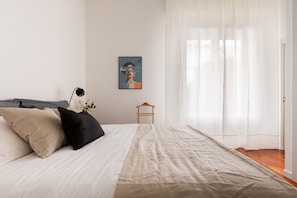 A neatly made bed with a beige and black pillow, a wooden hanger, and a framed picture on the wall. - Corso Garibaldi - Modern & Cozy Suite by Rentopolis (Milan)