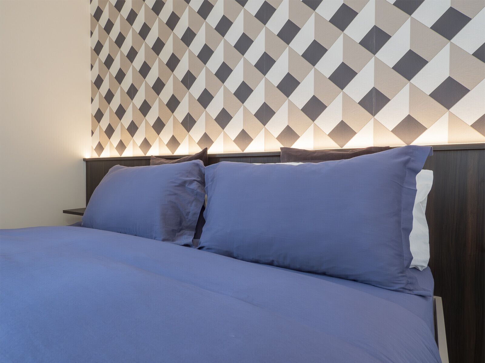 Un letto con testiera appoggiata a una parete con motivo geometrico.