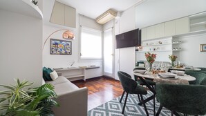 A modern living room with a sofa, a dining area with a table set for four, and a kitchen with cabinets and a TV. - Modern Split Level Apartment (Milan)