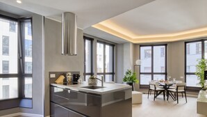 Een moderne keuken met een centraal eiland, grote ramen en een eethoek met een tafel en stoelen.