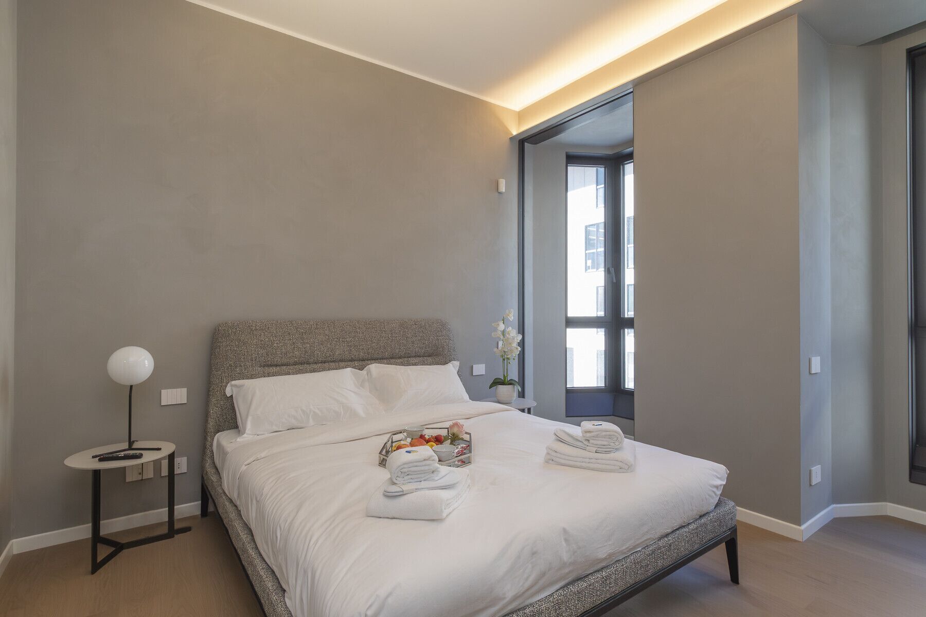A modern hotel room with a large bed, a bedside table, and a window with a view of the city.