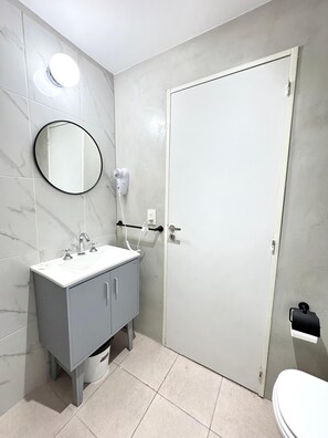 Kylpyhuone, jossa on valkoinen pesuallas, peili ja wc-istuin.