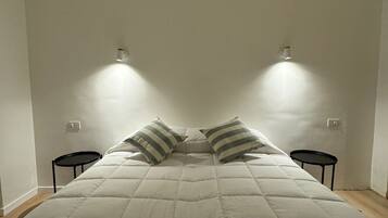 Una cama con edredón blanco acolchado, dos almohadas a rayas y dos mesitas de noche negras.