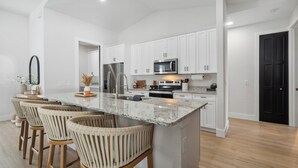 A modern kitchen with white cabinets, a central island with bar stools, stainless steel appliances, and a wooden floor.