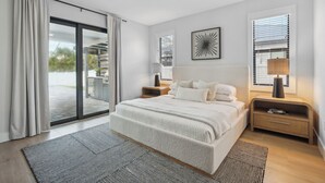 A modern bedroom with a large bed, a ceiling fan, and a view of the outdoors.