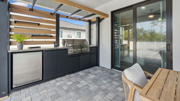 A modern outdoor kitchen with a built-in grill, a refrigerator, and a dining area with a table and chairs.