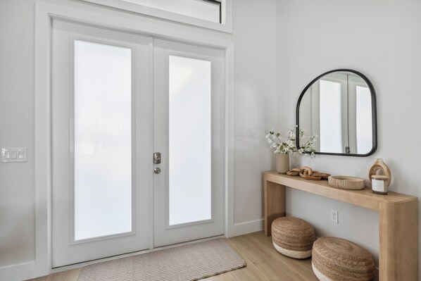 A modern interior with a double door, a wooden console table with decorative items, and a mirror.