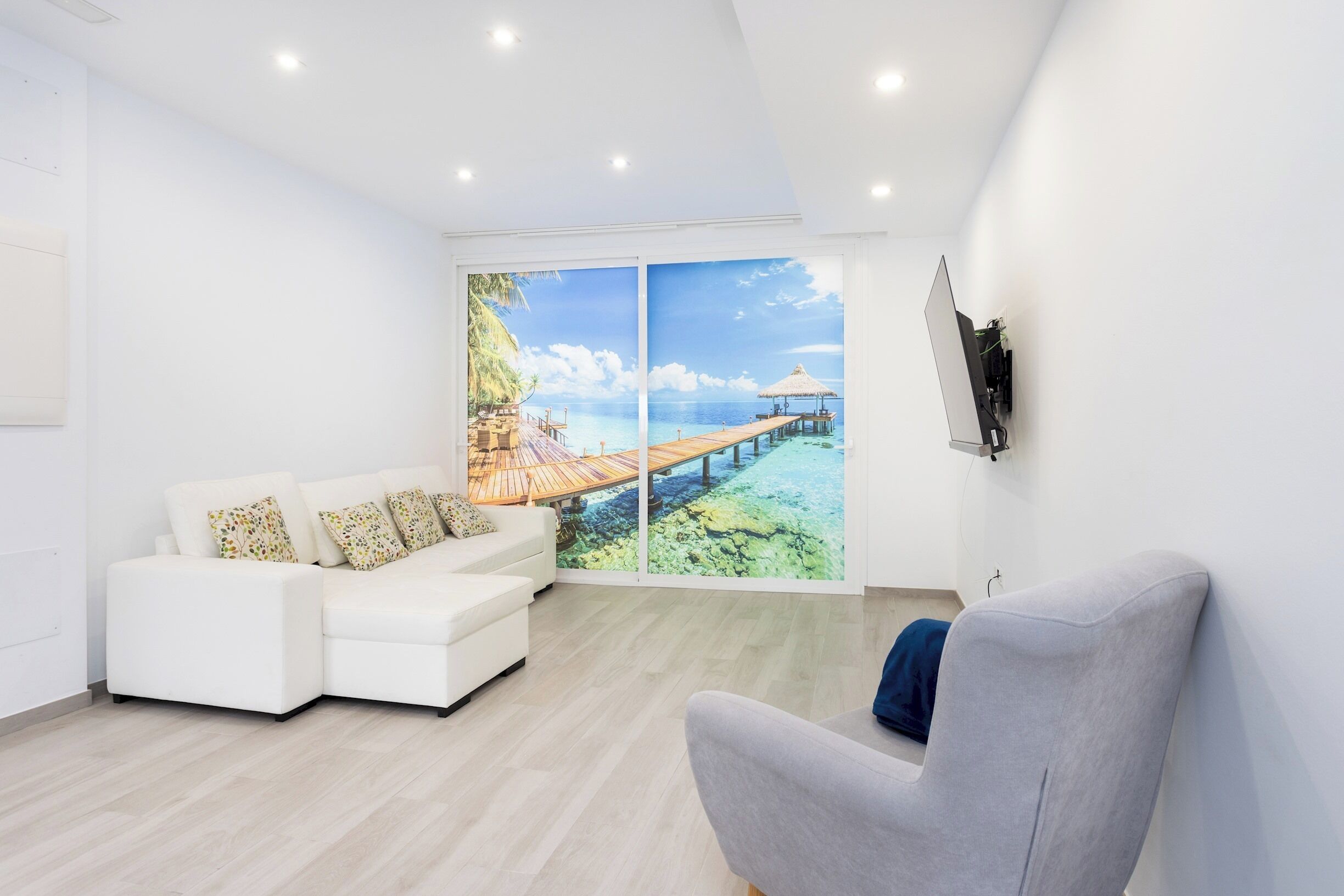 Un salón moderno con un sofá blanco, un sillón gris y un ventanal con vistas a un paisaje tropical.