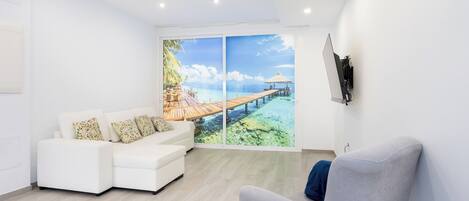Un salón moderno con un sofá blanco, un sillón gris y un ventanal con vistas a un paisaje tropical.