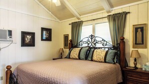 A bedroom with a wooden bed, two bedside tables, a window with curtains, and framed pictures on the wall. - Cozy Mockingbird Cottage (Eureka Springs)