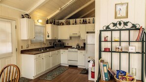 A kitchen with white cabinets, a microwave, stove, and a bookshelf with snacks. - Cozy Mockingbird Cottage (Eureka Springs)