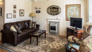 A cozy living room with a brown leather sofa, a wooden coffee table, a patterned rug, a fireplace, and a television. - Cozy Mockingbird Cottage (Eureka Springs)