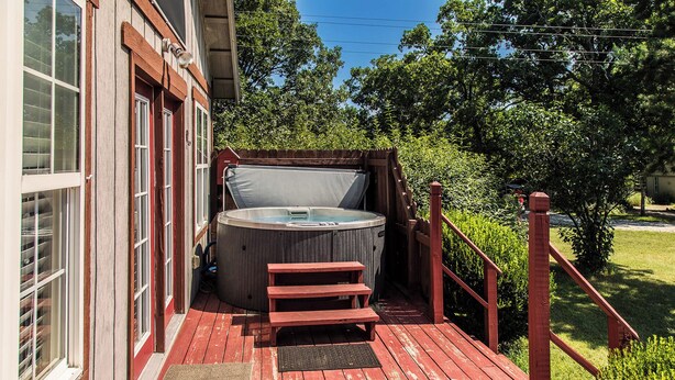 A hot tub on a wooden deck with steps leading up to it, surrounded by a wooden fence and lush greenery. - Cozy Mockingbird Cottage (Eureka Springs)