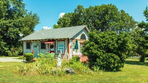 A small, single-story house with a porch, surrounded by lush greenery and trees. - Cozy Mockingbird Cottage (Eureka Springs)