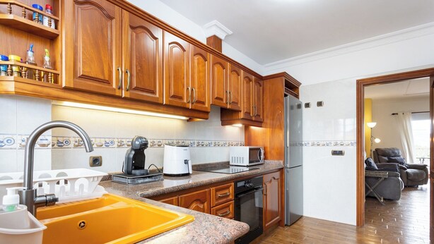 Eine Küche mit Holzausstattung, einem gelben Spülbecken, einer Mikrowelle und einem Kühlschrank.