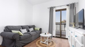Un moderno salón con un sofá gris, una pequeña mesa blanca y un televisor sobre un mueble blanco.