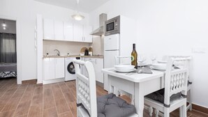 Una cocina moderna con armarios blancos, horno integrado y microondas. Hay una mesa de comedor con sillas y una botella de vino encima.