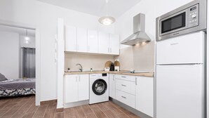 Una cocina compacta con armarios blancos, lavadora integrada, microondas y refrigerador.
